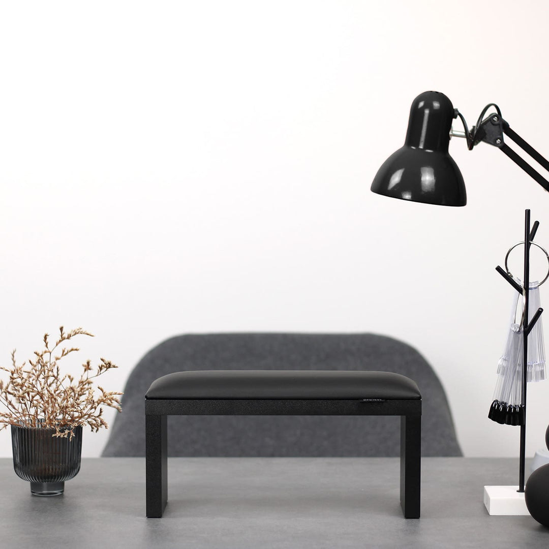 SPENVI Classic manicure arm rest with black leather cushion and black legs on modern salon desk under white lamp.