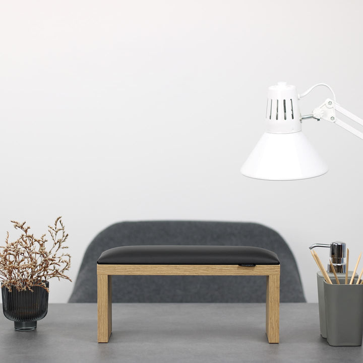 SPENVI Classic manicure arm rest with black leather cushion and oak-finish legs on modern salon desk under white lamp. #color_black