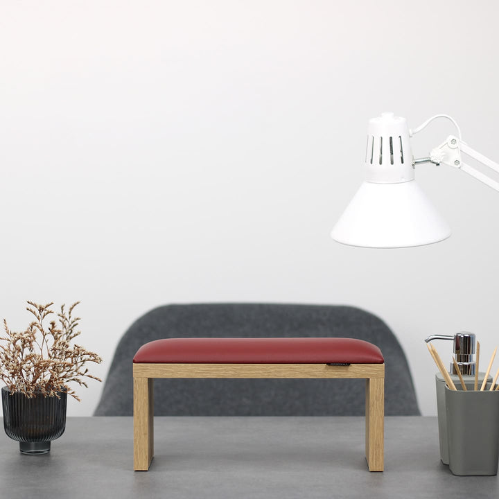 SPENVI Classic manicure arm rest with red leather cushion and oak-finish legs on modern salon desk under white lamp. #color_bordo
