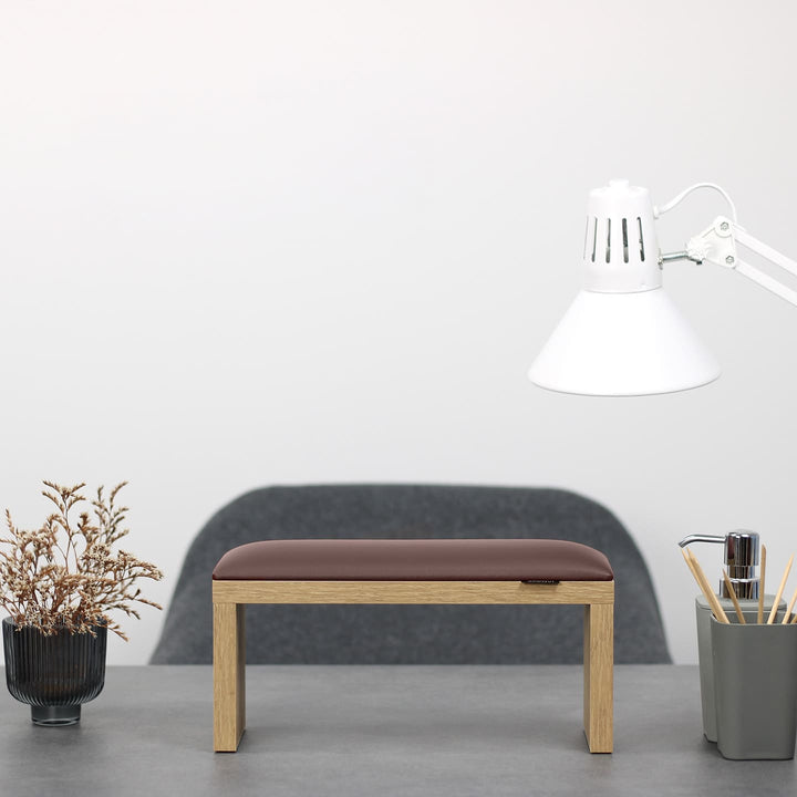 SPENVI Classic manicure arm rest with chocolate leather cushion and oak-finish legs on modern salon desk under white lamp. #color_chocolate