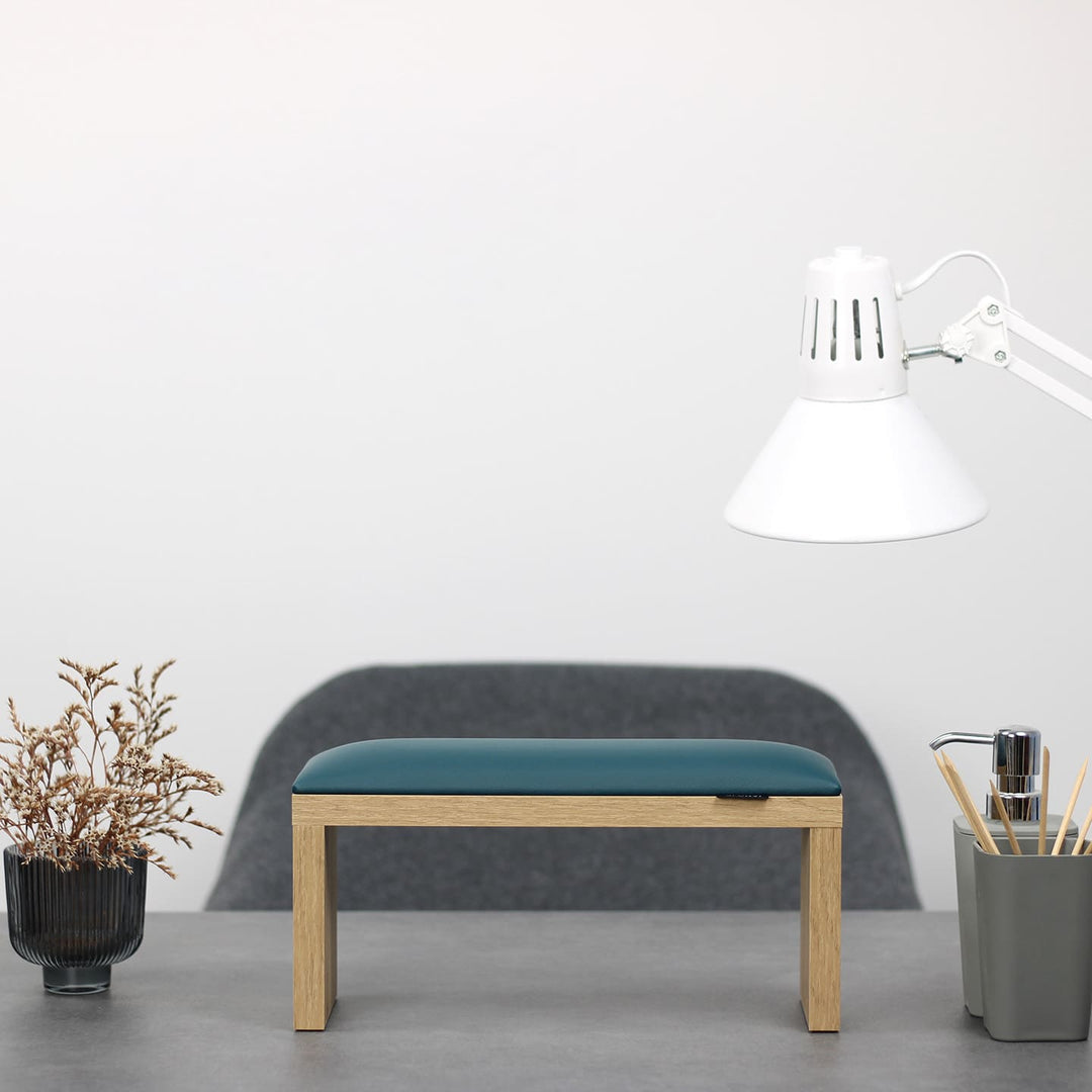 SPENVI Classic manicure arm rest with dark green leather cushion and oak-finish legs on modern salon desk under white lamp. #color_dark-green