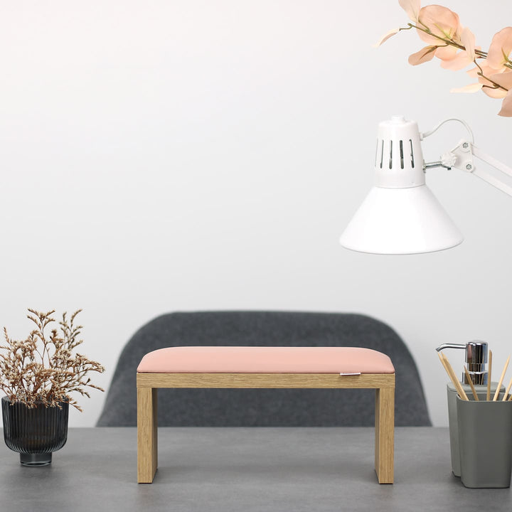 SPENVI Classic manicure arm rest with light pink leather cushion and oak-finish legs on modern salon desk under white lamp. #color_light-pink