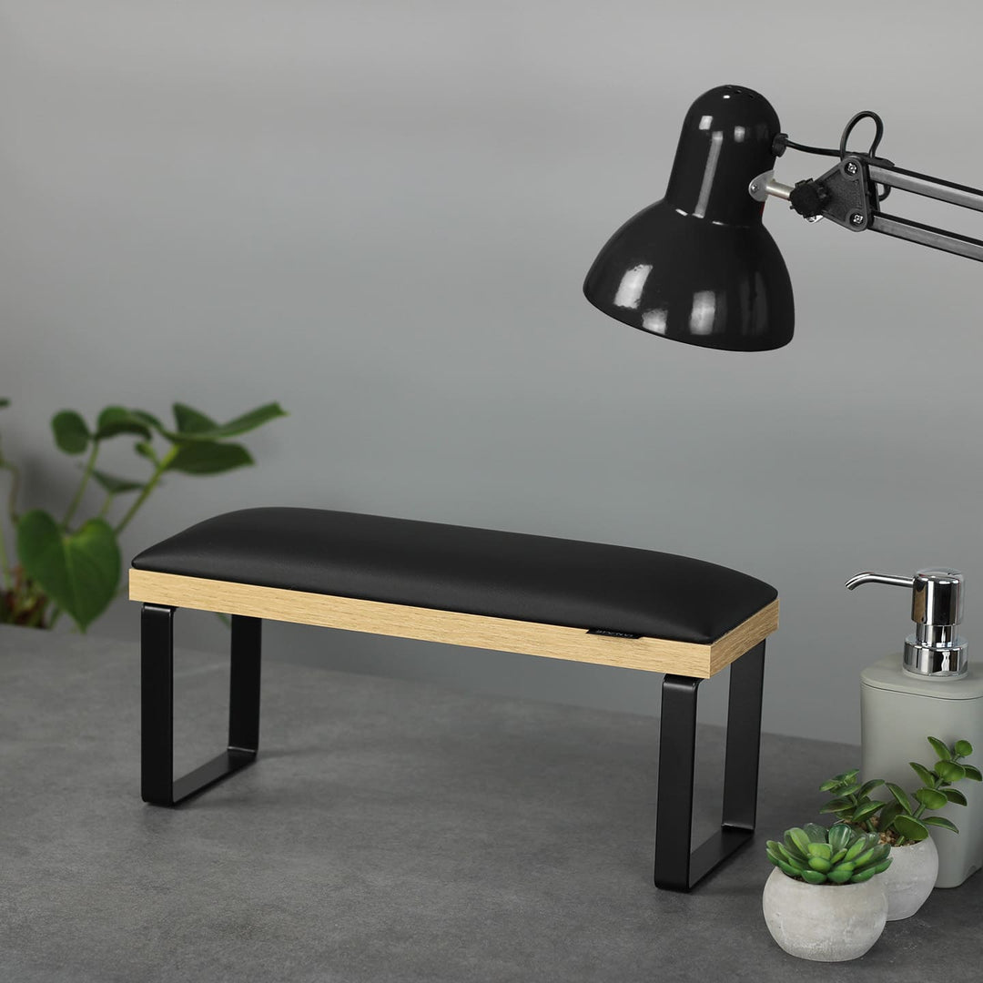 SPENVI Loft manicure arm rest with black leather cushion, oak-finish base, and black metal legs on modern salon desk with lamp and plants. #color_black