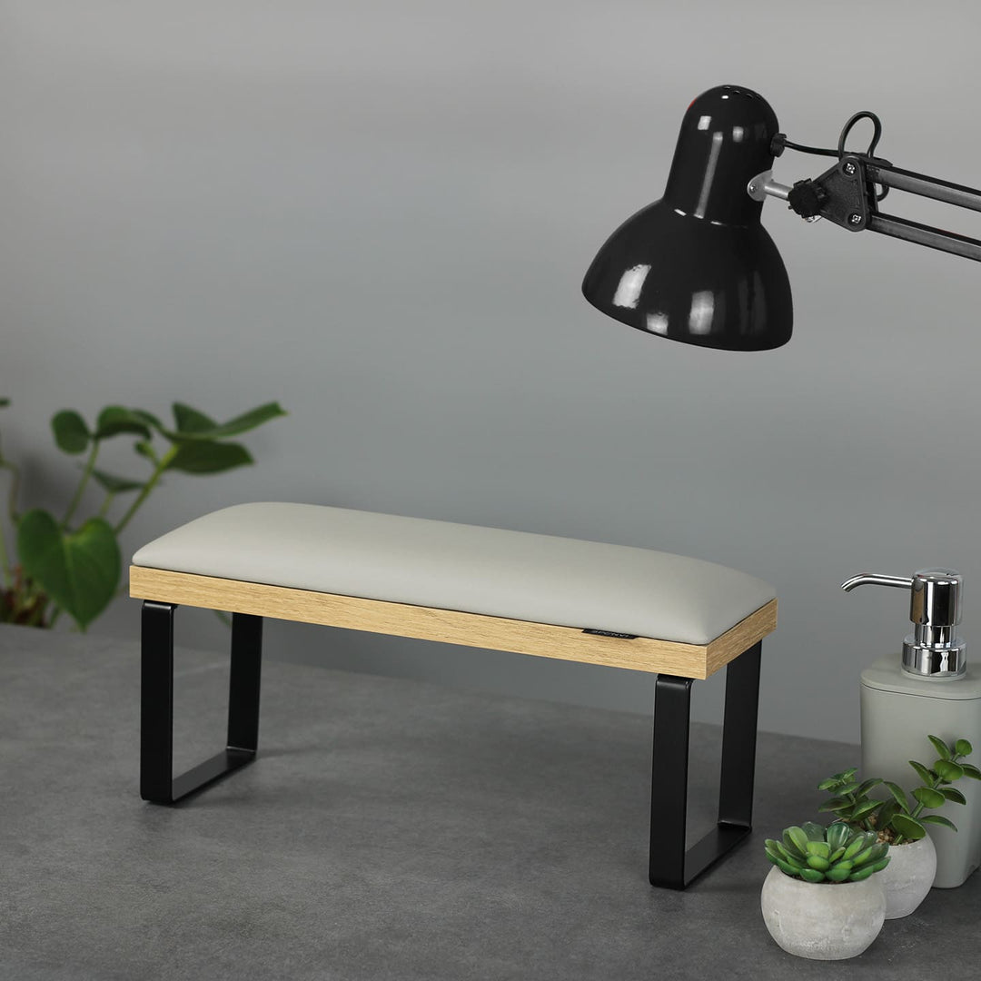 SPENVI Loft manicure arm rest with light gray leather cushion, oak-finish base, and black metal legs on modern salon desk with lamp and plants. #color_cloud