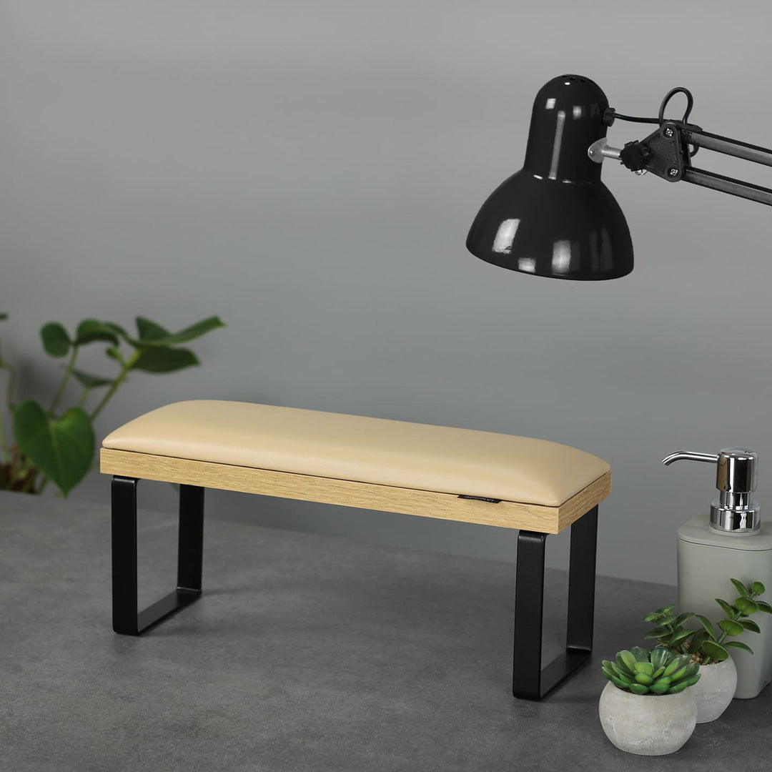 SPENVI Loft manicure arm rest with beige leather cushion, oak-finish base, and black metal legs on modern salon desk with lamp and plants. #color_coffee-milk