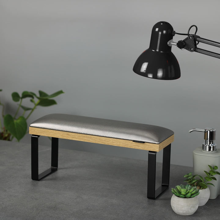 SPENVI Loft manicure arm rest with graphite leather cushion, oak-finish base, and black metal legs on modern salon desk with lamp and plants. #color_graphite