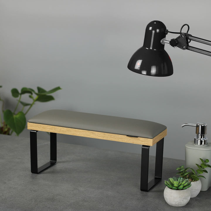 SPENVI Loft manicure arm rest with gray leather cushion, oak-finish base, and black metal legs on modern salon desk with lamp and plants. #color_gray