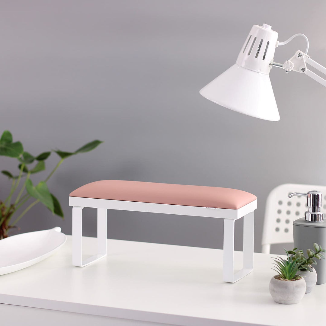 SPENVI Loft manicure arm rest with white leather cushion, white base, and white metal legs on modern salon desk with lamp and plants. #color_light-pink
