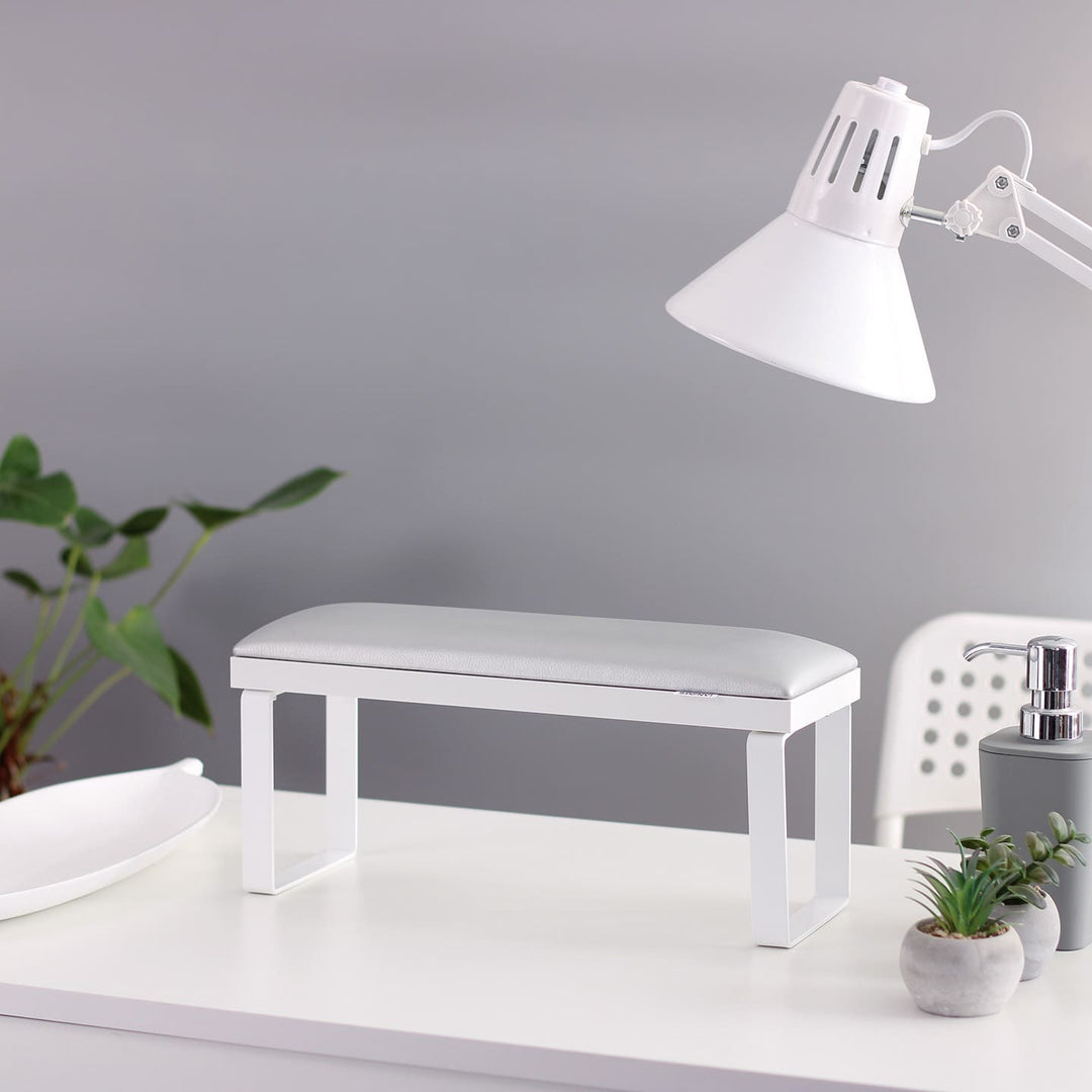 SPENVI Loft manicure arm rest with white leather cushion, white base, and white metal legs on modern salon desk with lamp and plants. #color_silver
