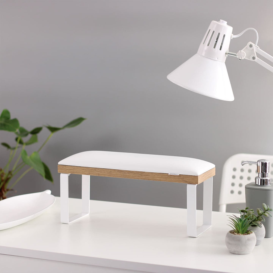 SPENVI Loft manicure arm rest with white leather cushion, oak-finish base, and white metal legs on modern salon desk with lamp and plants.