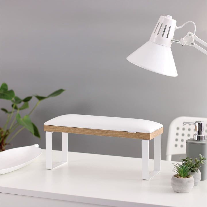 SPENVI Loft manicure arm rest with white leather cushion, oak-finish base, and white metal legs on modern salon desk with lamp and plants.