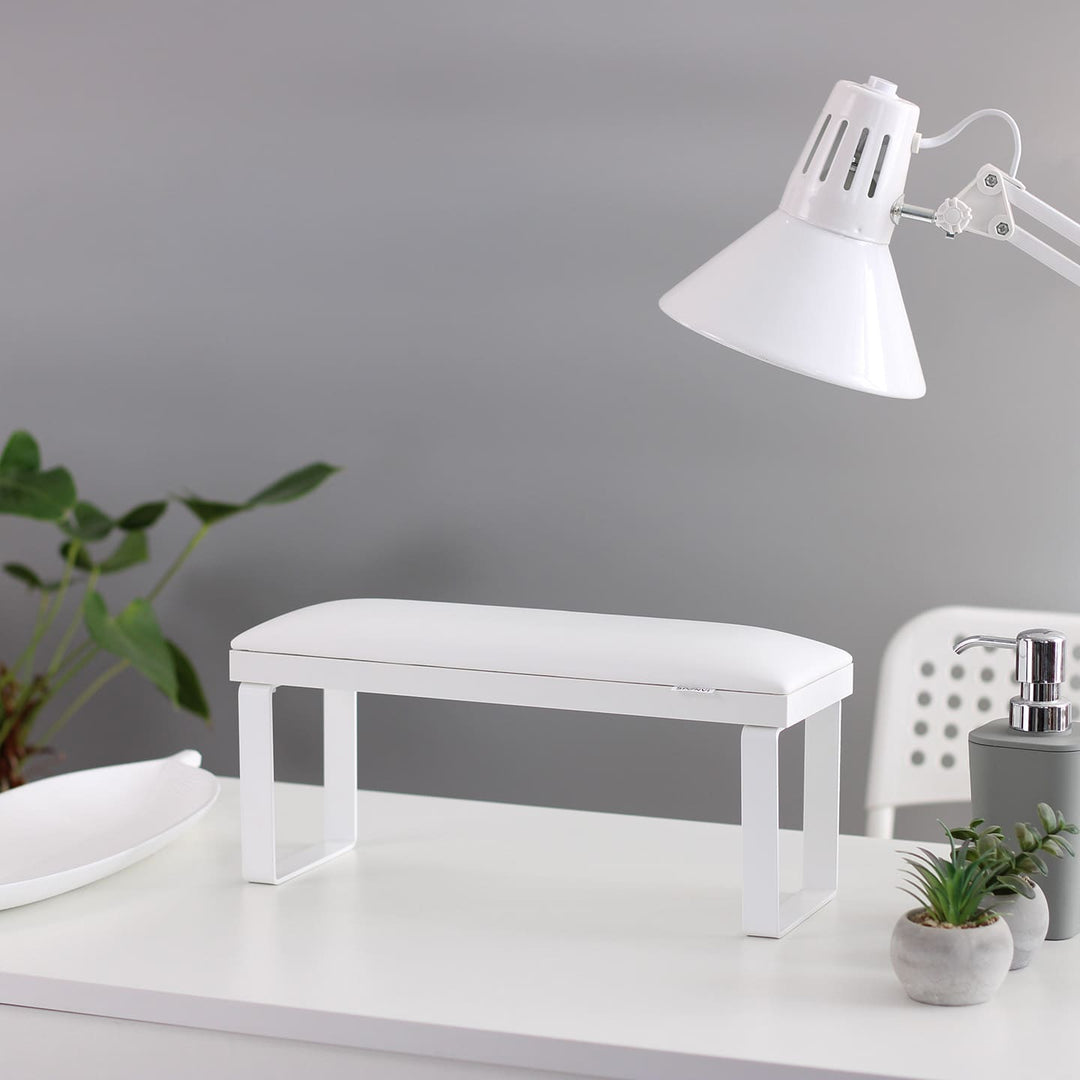 SPENVI Loft manicure arm rest with white leather cushion, white base, and white metal legs on modern salon desk with lamp and plants. #color_white